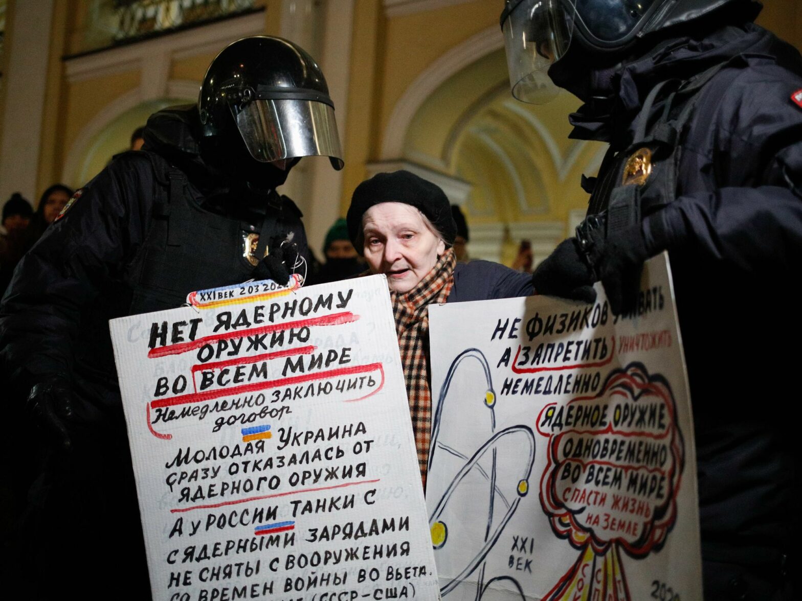 photo of police detaining elderly woman holding up a protest sign