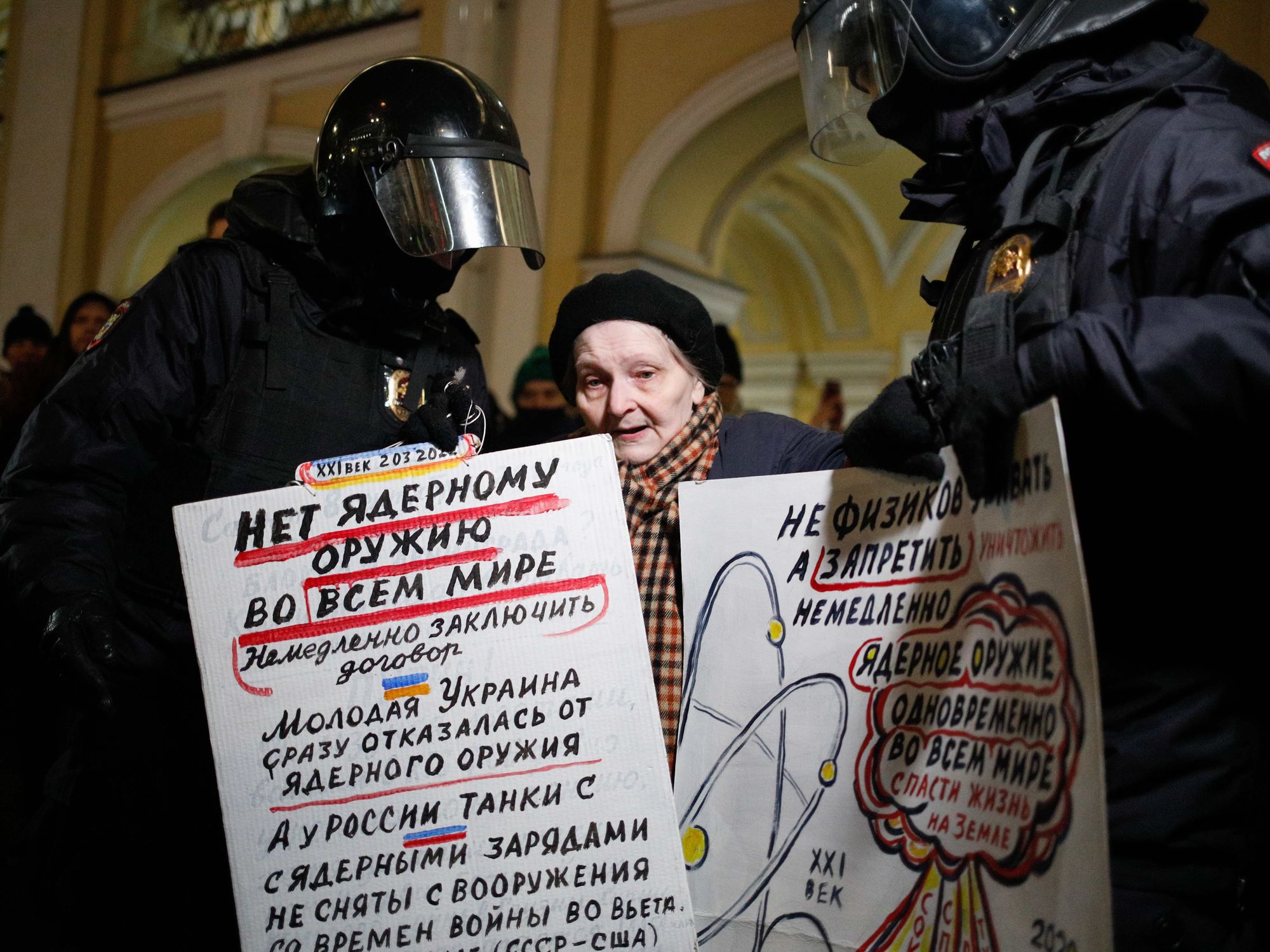 photo of police detaining elderly woman holding up a protest sign