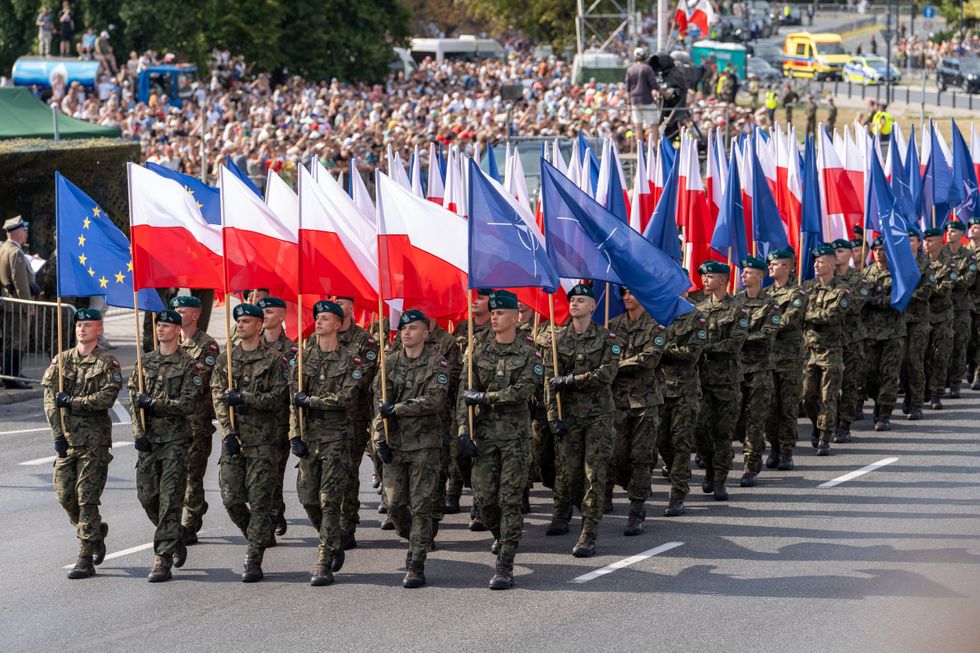 Photo of Polish soldiers marching with Polish and NATO flags in Warsaw on Aug. 15