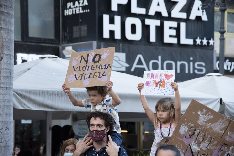 Photo of protesters carrying children on their shoulders. The children are holding signs with slogans against "vicarious violence" during a protest in Tenerife, Spain.