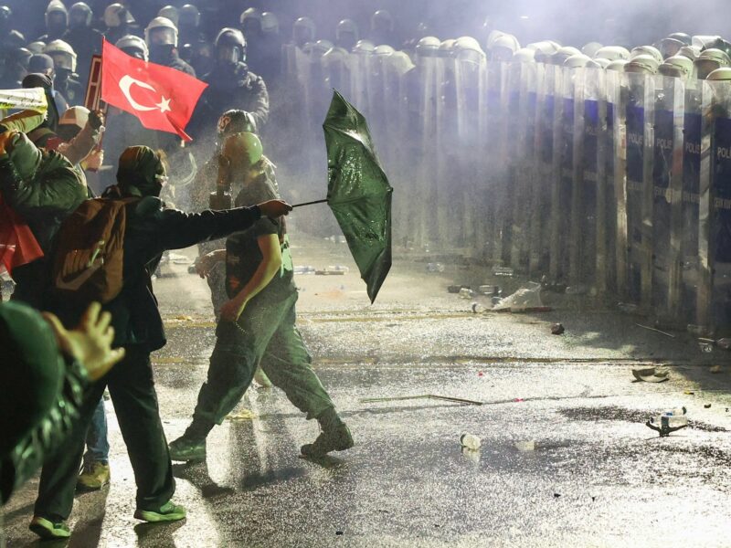 photo of protesters facing police with a turkish flag
