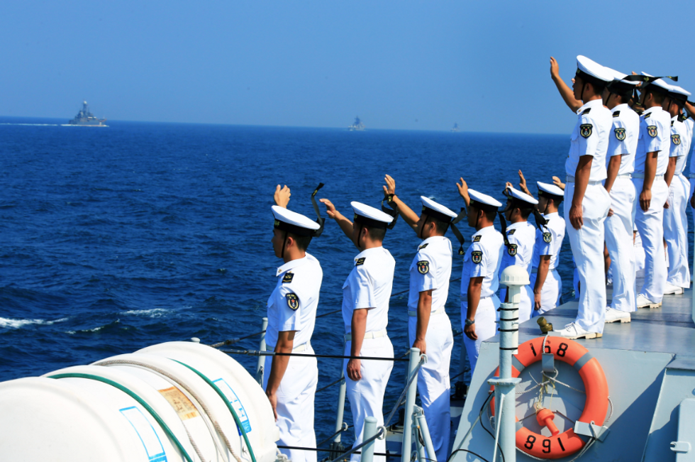 Photo of Russian and Chinese sailors waving aboard an aircraft carrier as they participate in military exercises in the South China Sea