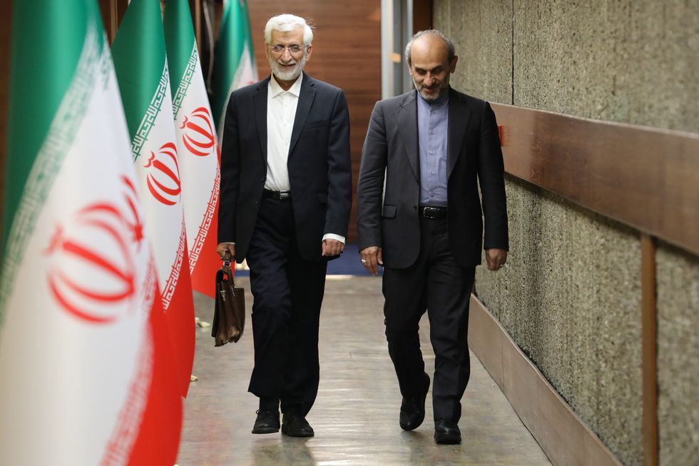 Photo of Saeed Jalili and Peyman Jebel walking down a hall with iran flags on poles spanning the left side of the hall