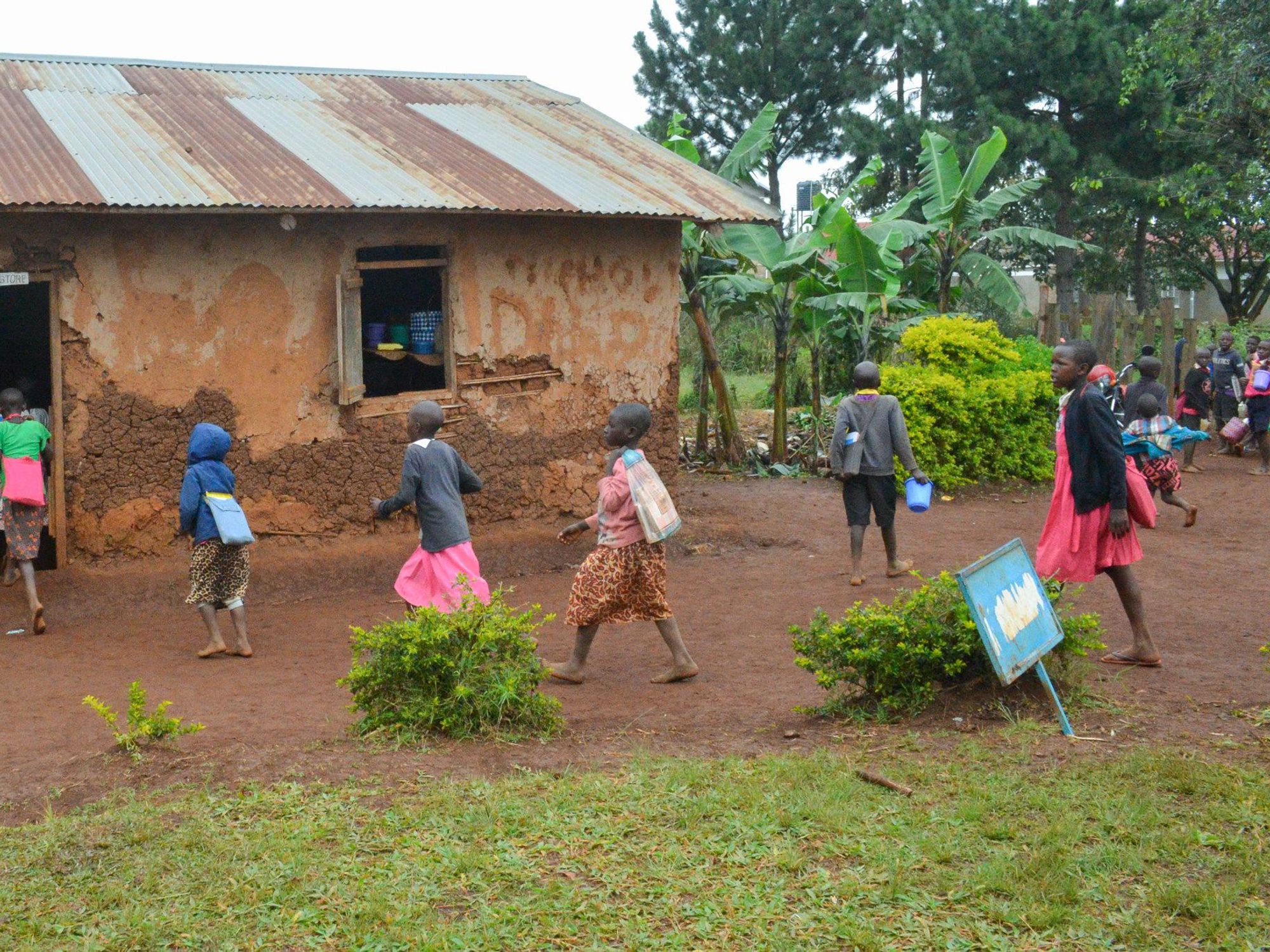 Photo of schoolchildren entering a mud-walled classroom at Kyeihara Integrated Primary School in Sheema, Uganda.