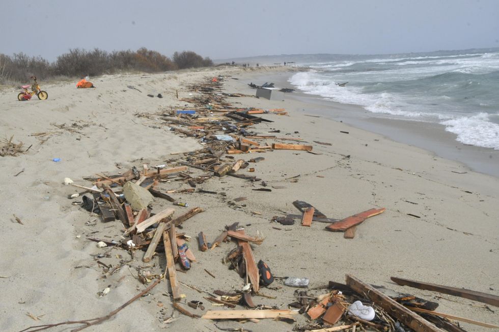 Photo of the remains of the boat carrying migrants washed up on the beach by the sea.