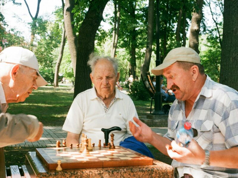 Photo of three elderly men playing chess in a park