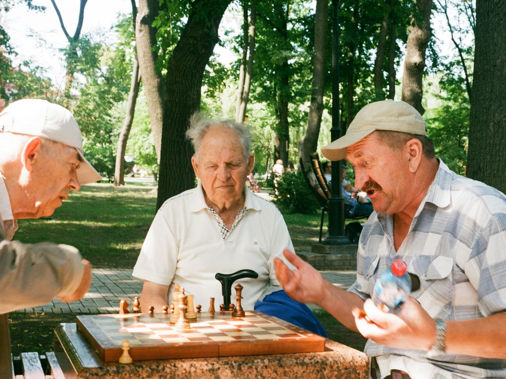 Photo of three elderly men playing chess in a park