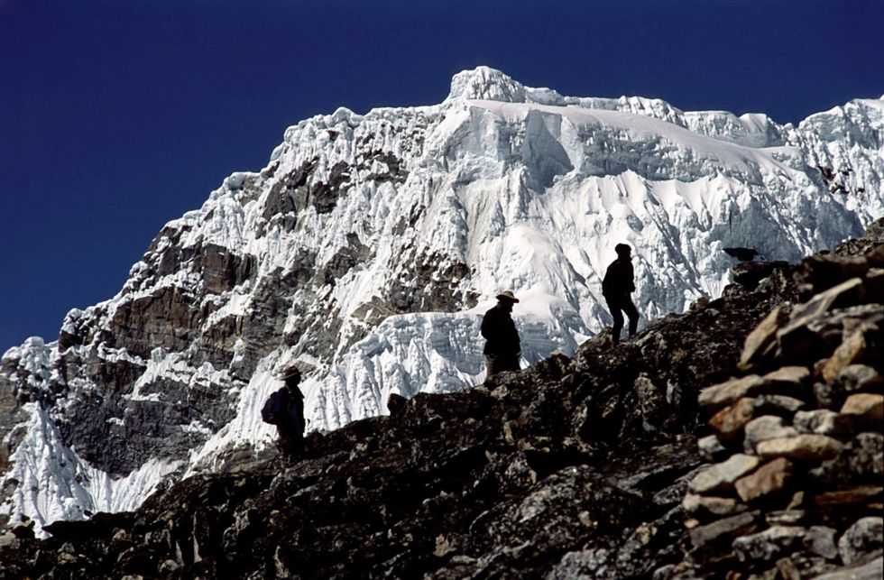 Photo of three silhouettes of tourists climbing up the Everest, with a mountainous backdrop