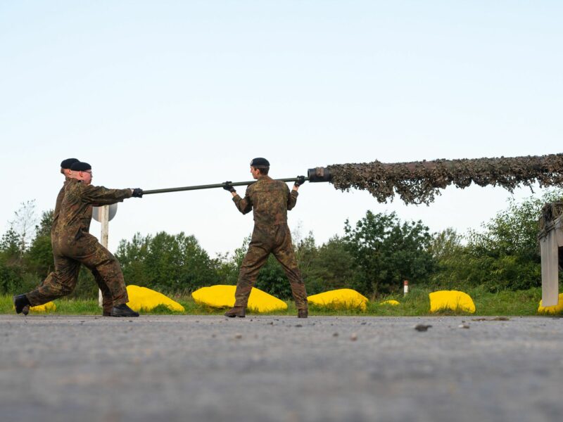 Photo of three soldiers of the German Armed Forces cleaning the cannon of a Leopard 2 A7V battle tank.