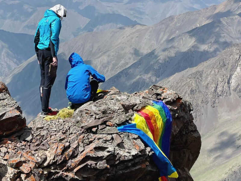 Photo of to climbers next to a rainbow flag and a Ukrainian flag on Vladimir Putin Peak, Kyrgyzstan