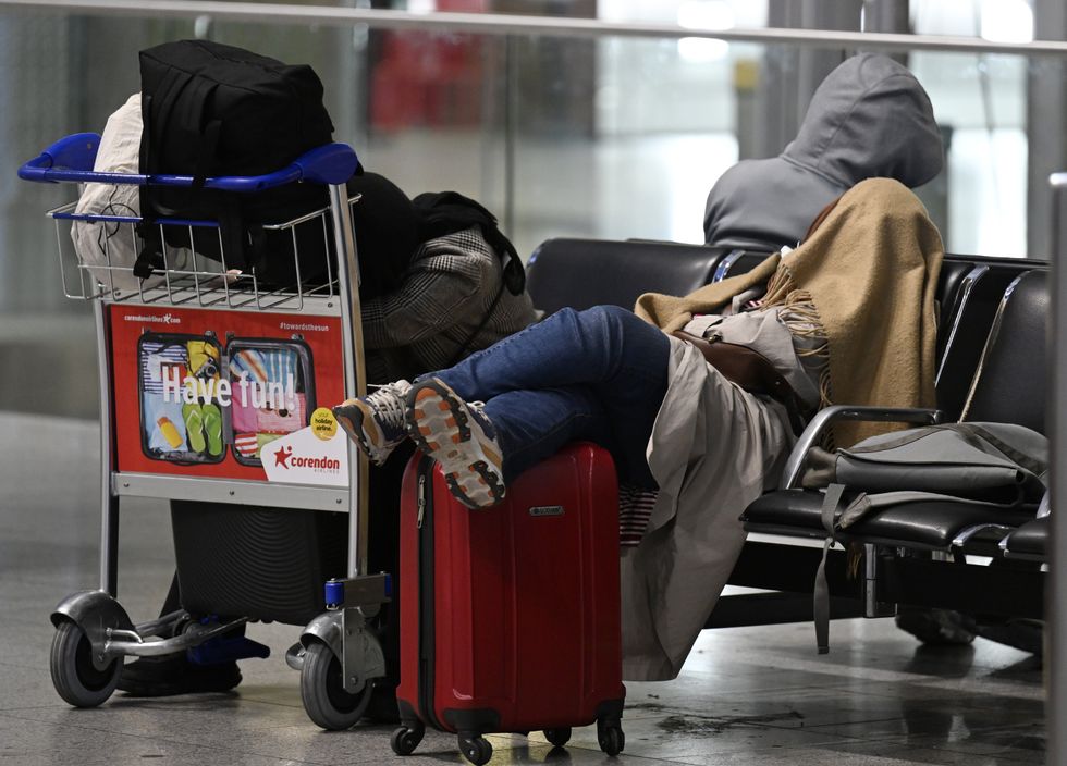 photo of travelers sleeping in the terminal next to their suitcases. Their faces are covered by blankets.