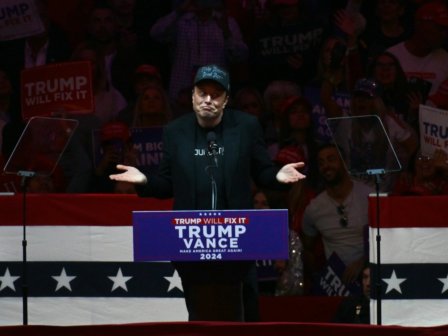 photo of trump speaking at lectern with trump poster