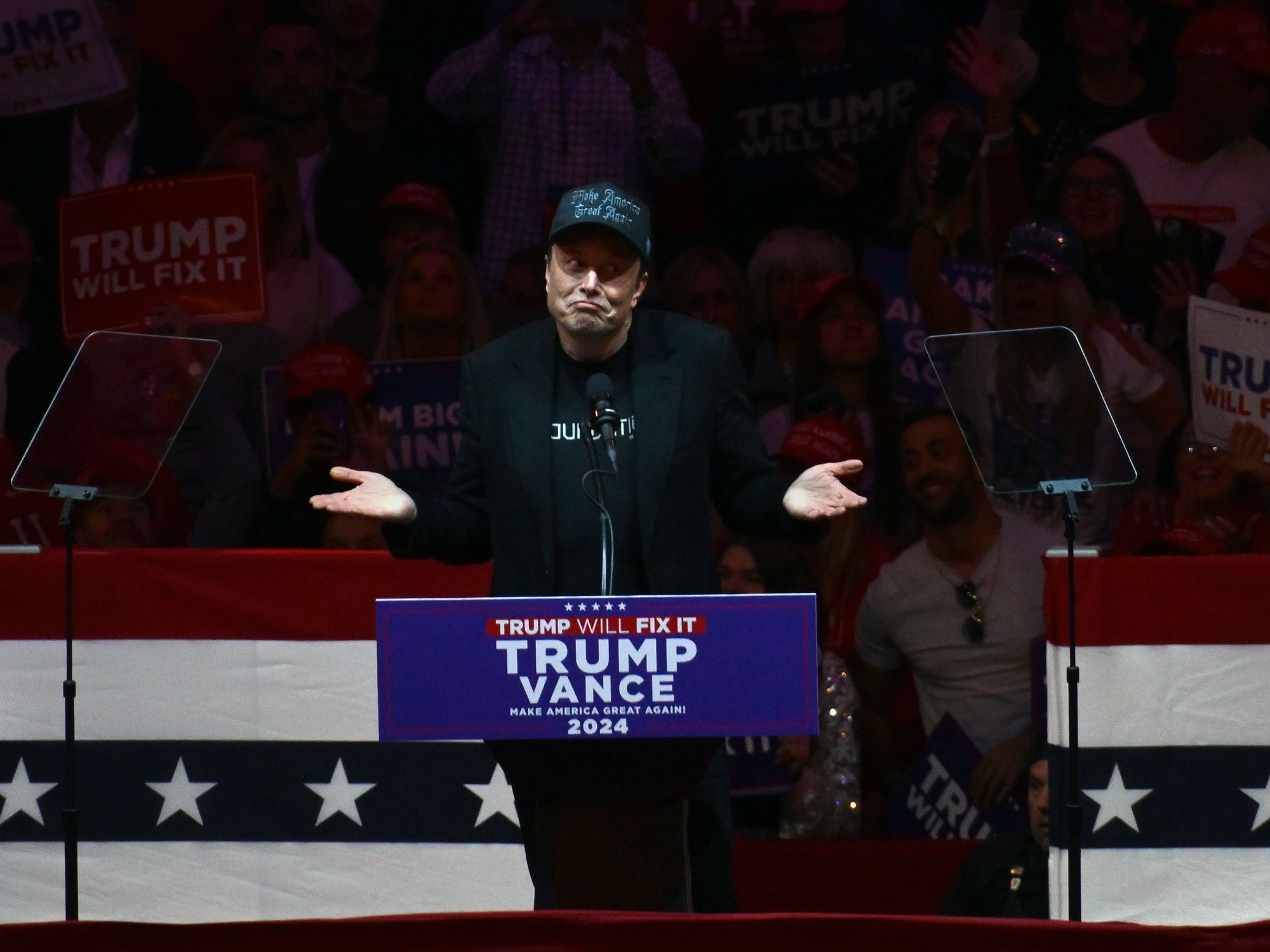 photo of trump speaking at lectern with trump poster