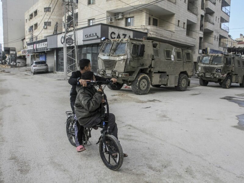 Photo of two kids on a bike in front of Israeli military vehicles roaming the streets of Jenin city on November 20.