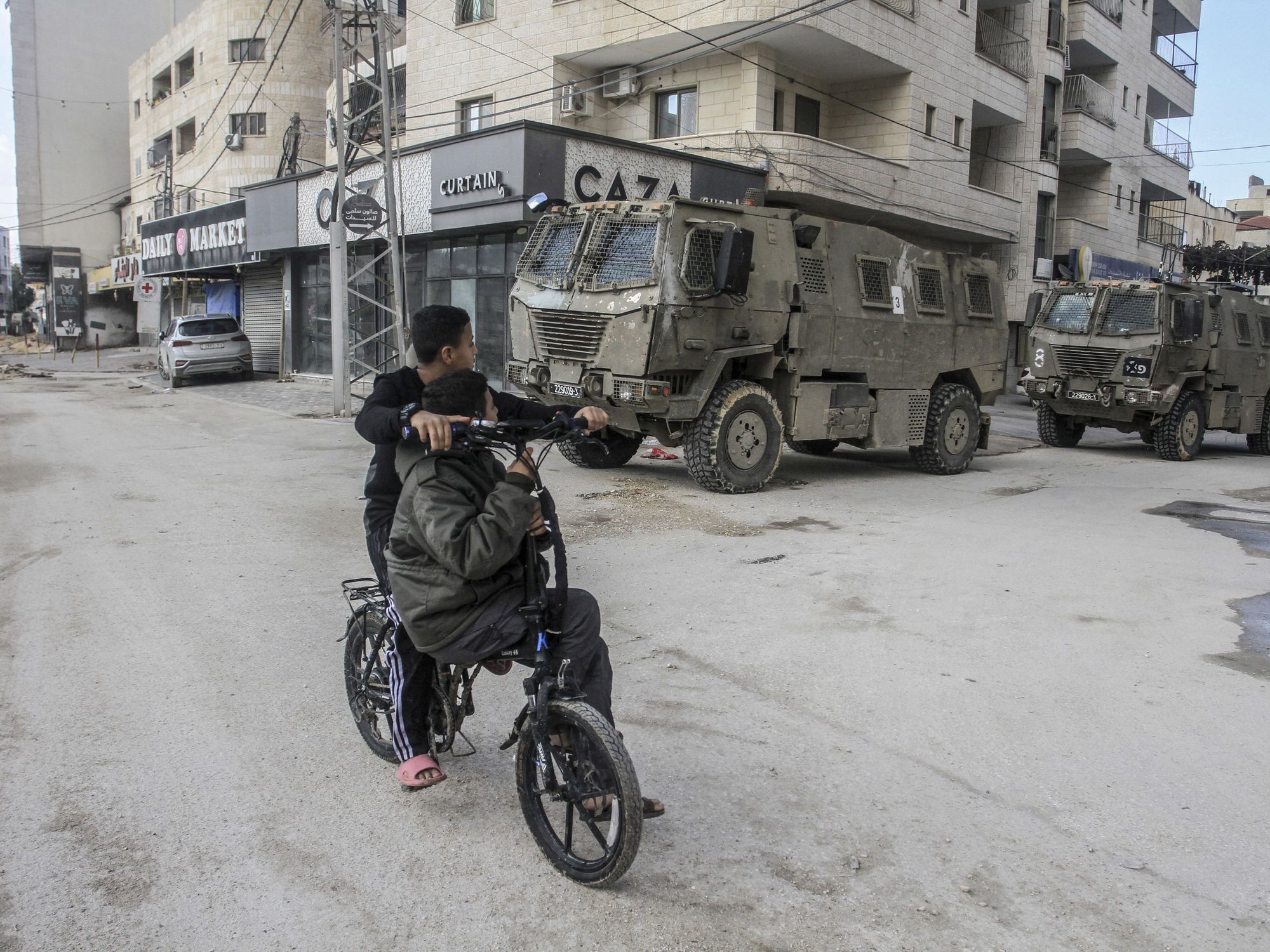Photo of two kids on a bike in front of Israeli military vehicles roaming the streets of Jenin city on November 20.
