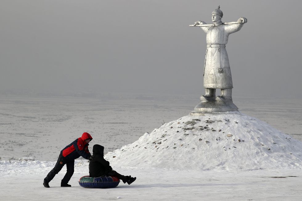 photo of two kids playing in the snow with a religious statue