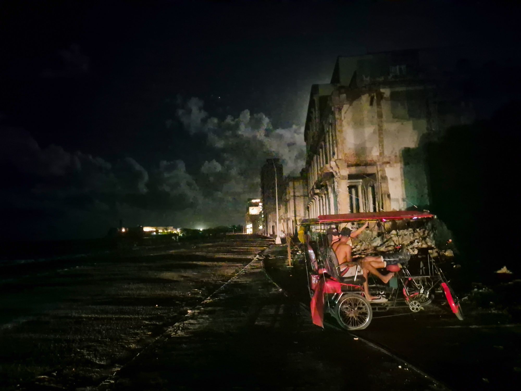 Photo of two men sitting in a bicycle cab during a power cut in Cuba.