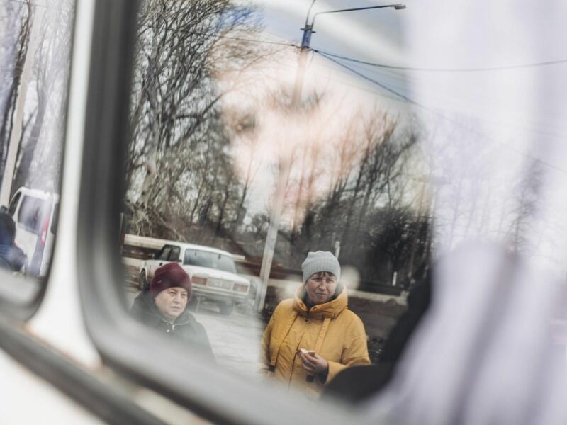 Photo of two mothers in Lisichansk, Ukraine, look at the bus as they send their children to the west of the country.