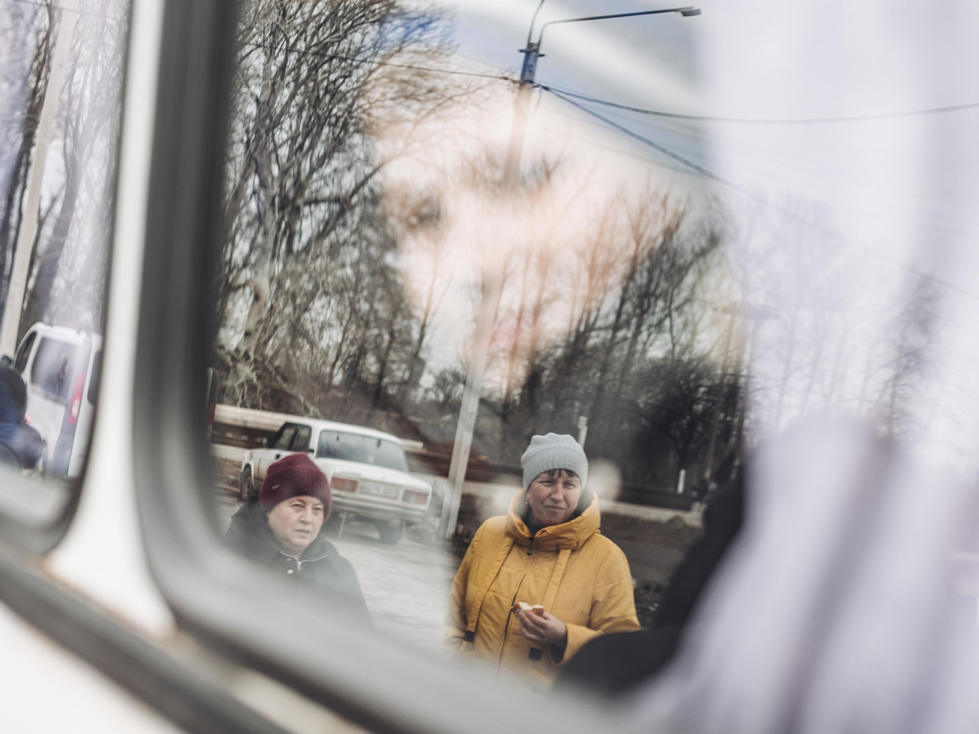 Photo of two mothers in Lisichansk, Ukraine, look at the bus as they send their children to the west of the country.