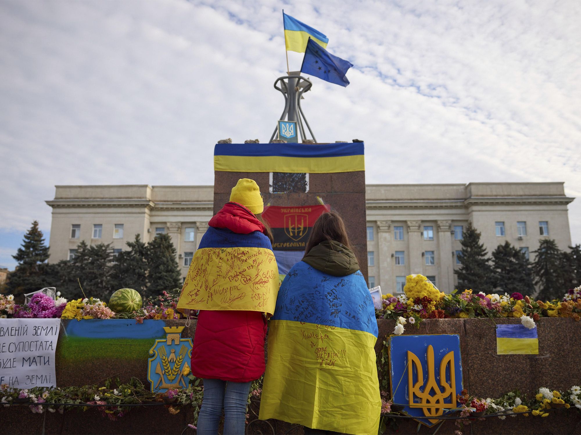 photo of two people at a memorial in Kherson with Ukraine flag draped over them