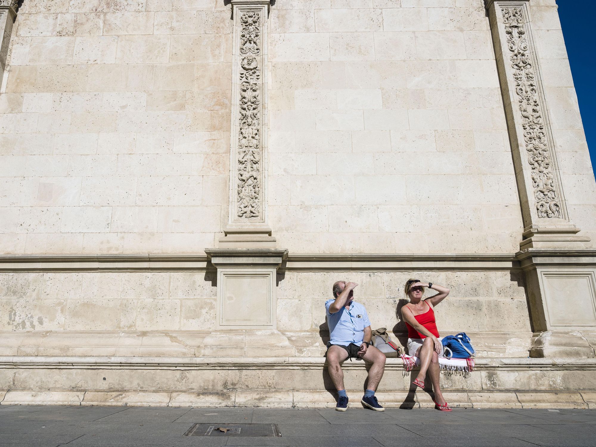 photo of two people sitting on a bench covering their eyes from the sun