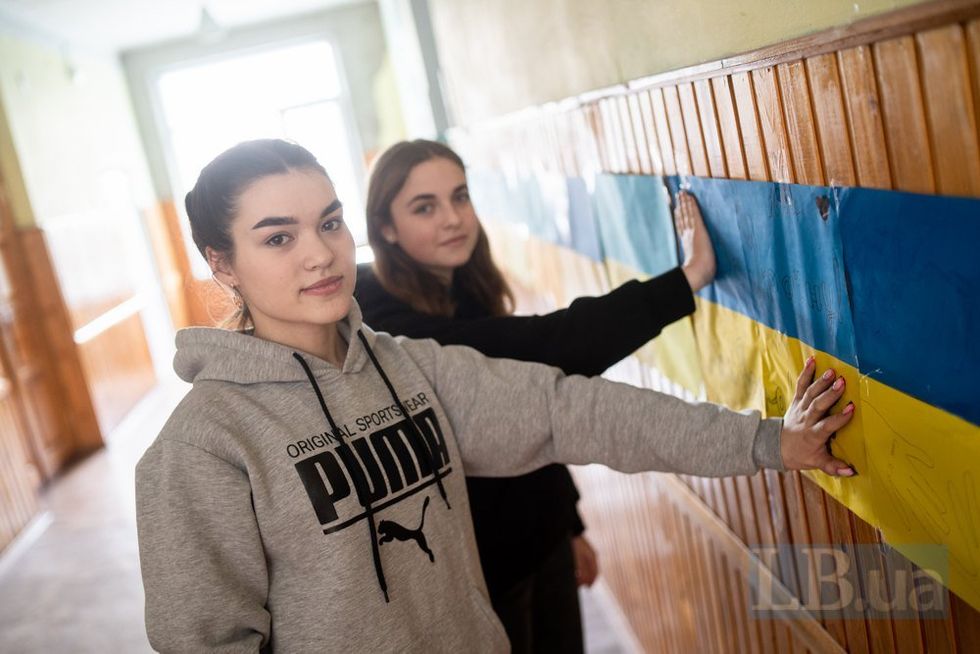 photo of two students touching a ukrainian flag on their school wall