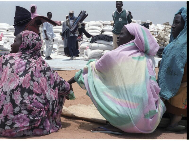 Photo of two women sat on the floor holding hands in a refugee camp near the town of Nyala, Darfur, Sudan.