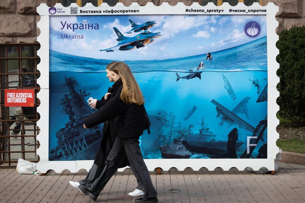 Photo of two women walking by a mural in Kyiv depicting Ukrainian victories in the Black Sea, in central Kyiv.
