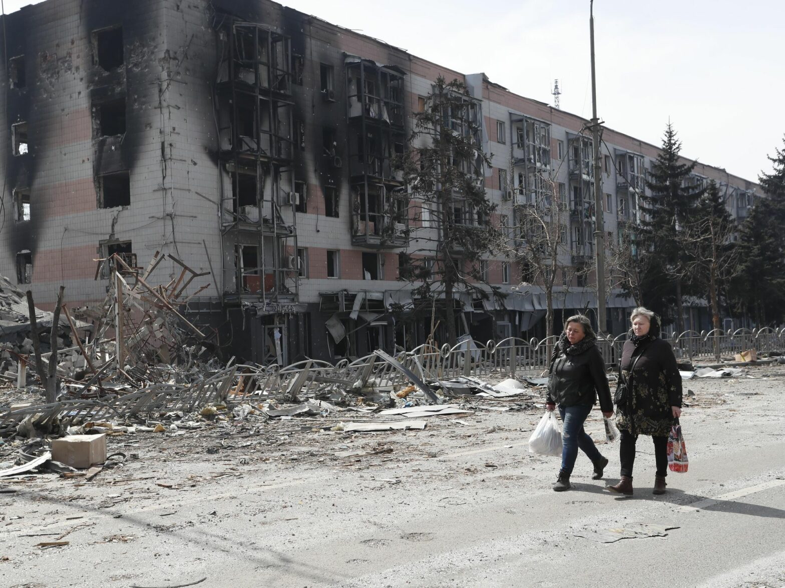 Photo of two women walking past a building in Mariupol, Ukraine, after it was hit by Russian shelling.