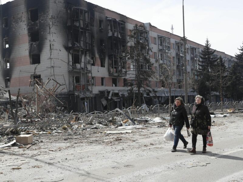 Photo of two women walking past a building in Mariupol, Ukraine, after it was hit by Russian shelling.
