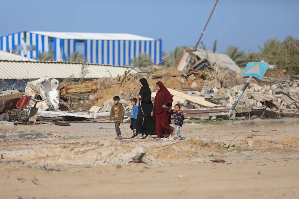 photo of two women walking with three children amid rubble