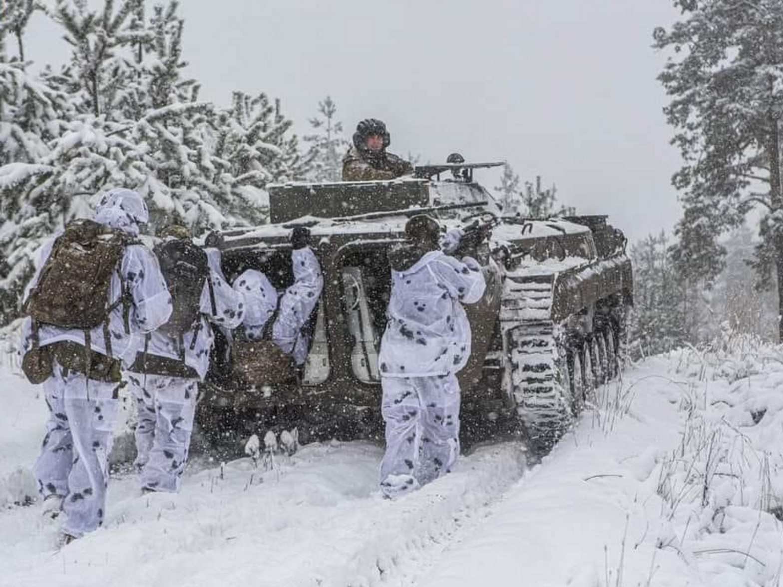 Photo of Ukrainian soldiers in winter gear, marching behind a tank in a snowy landscape