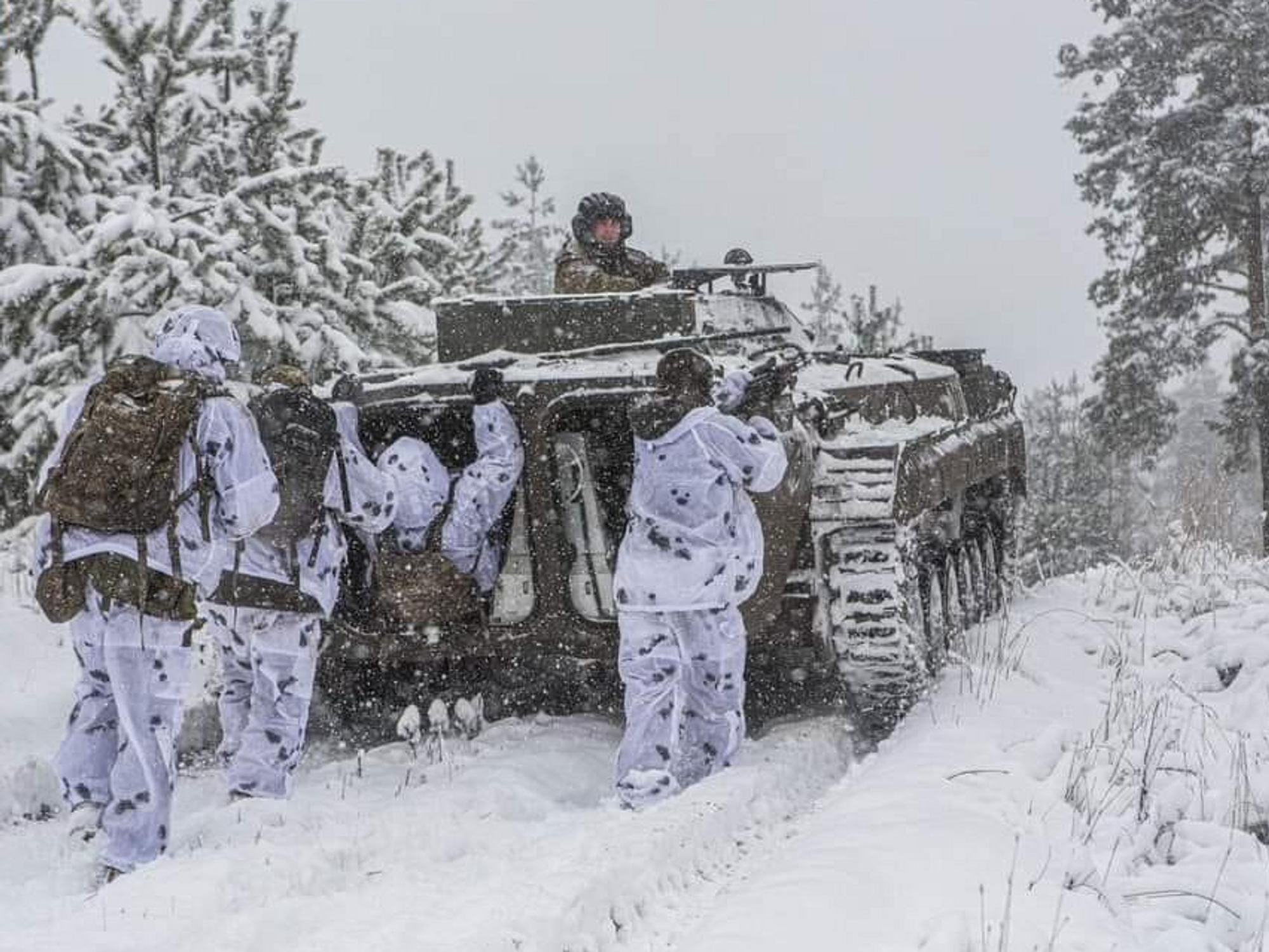 Photo of Ukrainian soldiers in winter gear, marching behind a tank in a snowy landscape