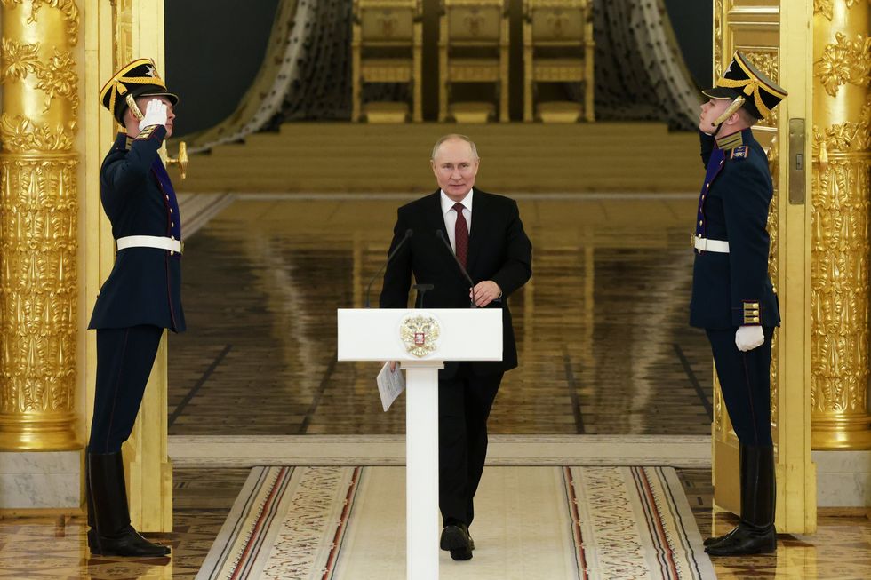 photo of vladimir putin walking to a white podium with two guards on either side.