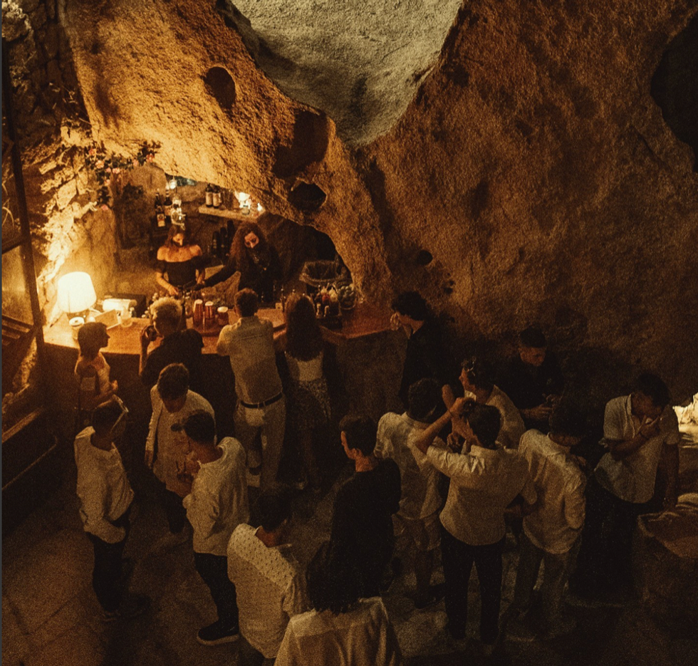Photo taken inside of the Ritual Club, where young people drink by the bar. The nightclub is set inside of a cave-like structure.