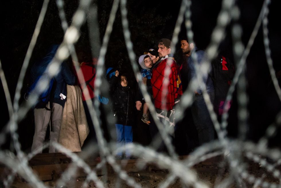 photo through barbed wire fence of syrian refugee adults and children