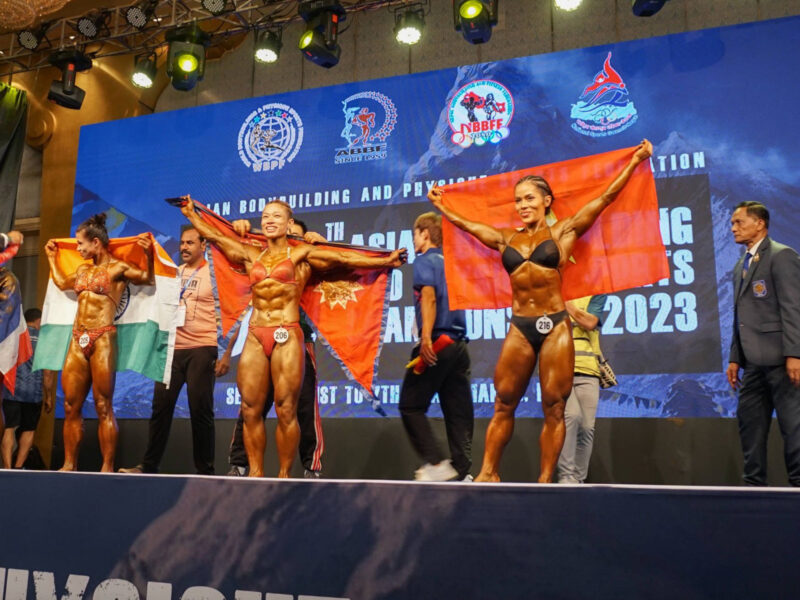 Photograoph of four female bodybuilders holding their country's flags on stage.