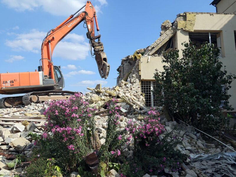 Photograph of a demolition vehicle removing rubble as works to restore the Central City Hospital.