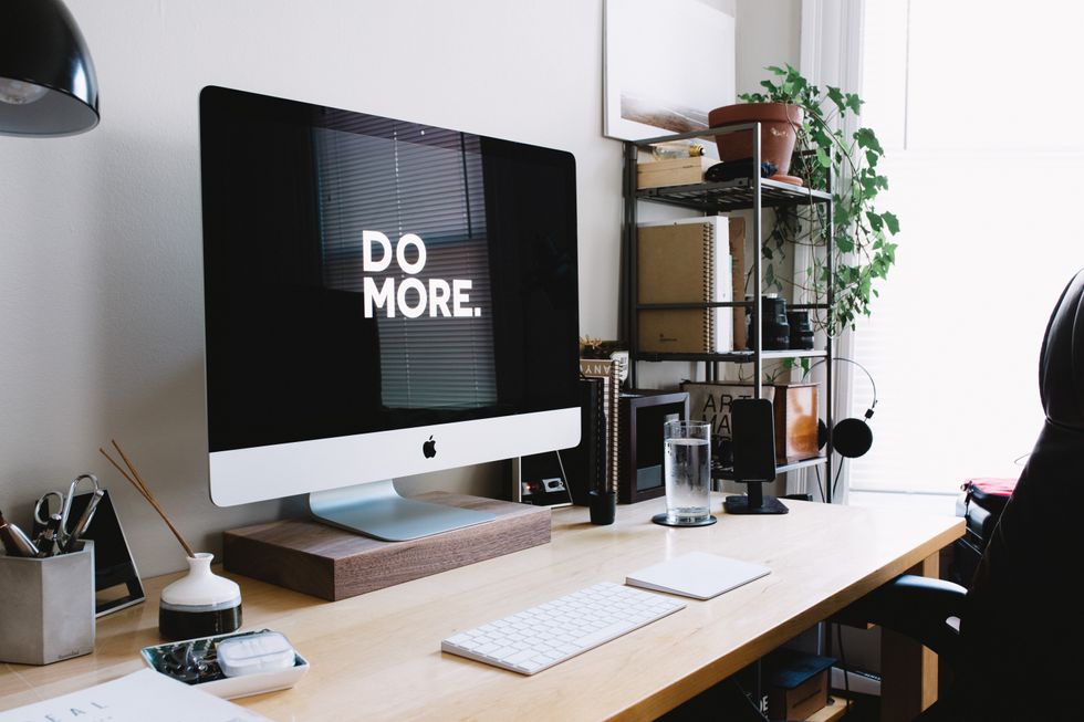 Photograph of a desk with a silver apple computer on it, which reads "Do More" on the screen.