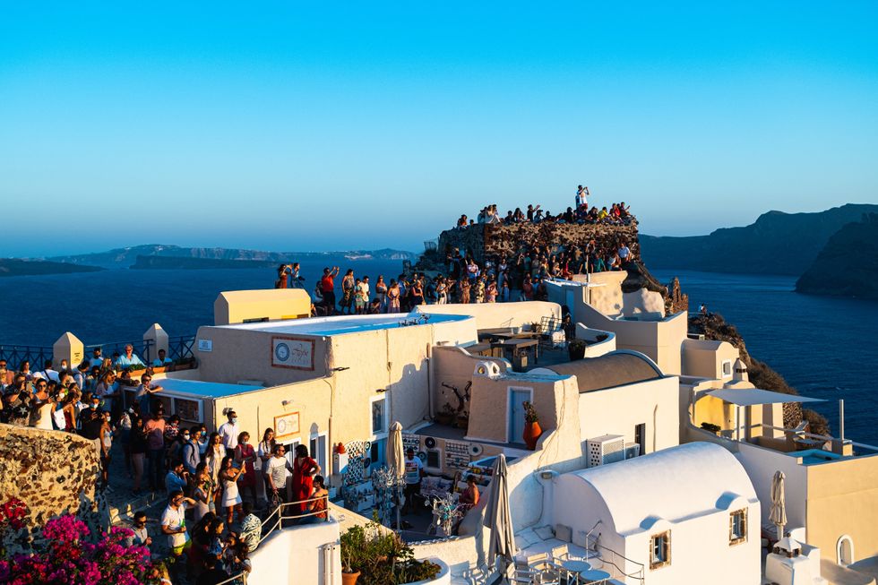 Photograph of a ​group of tourists standing on a cliffside in Santorini.