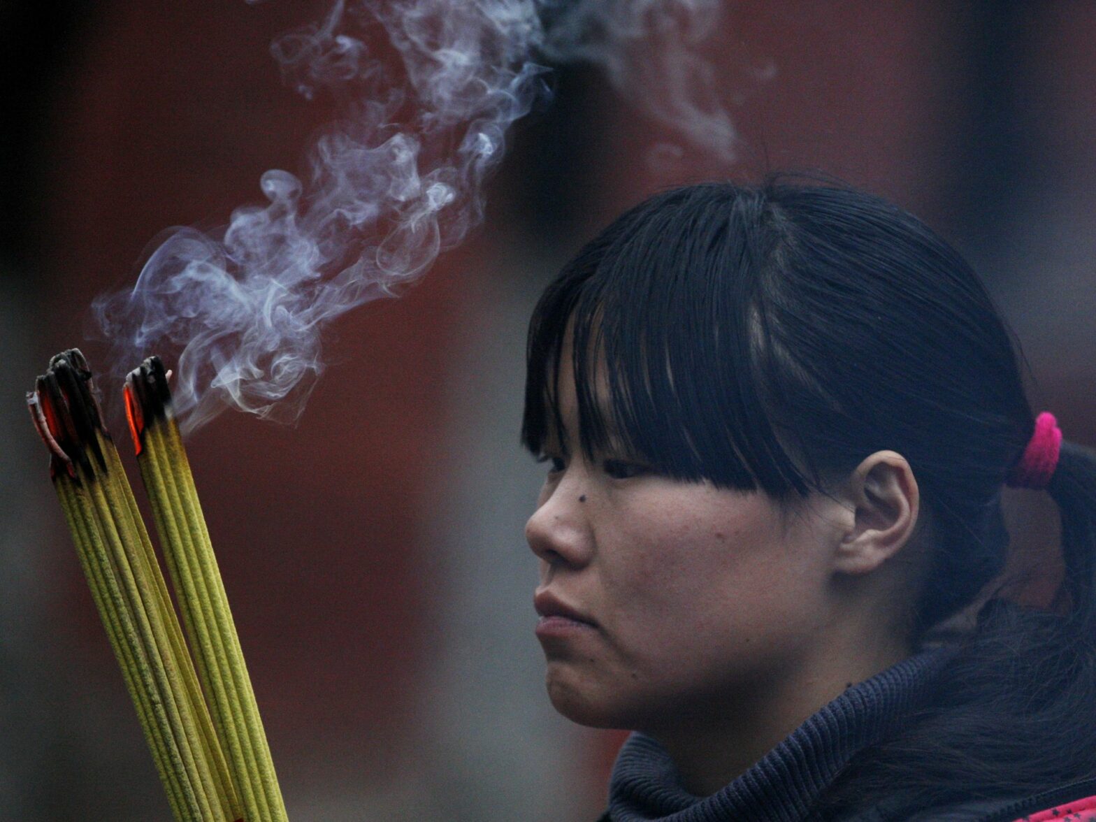 Photograph of a girl praying at a temple during Chinese Lunar New Year. She is burning incense.