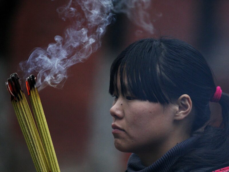 Photograph of a girl praying at a temple during Chinese Lunar New Year. She is burning incense.