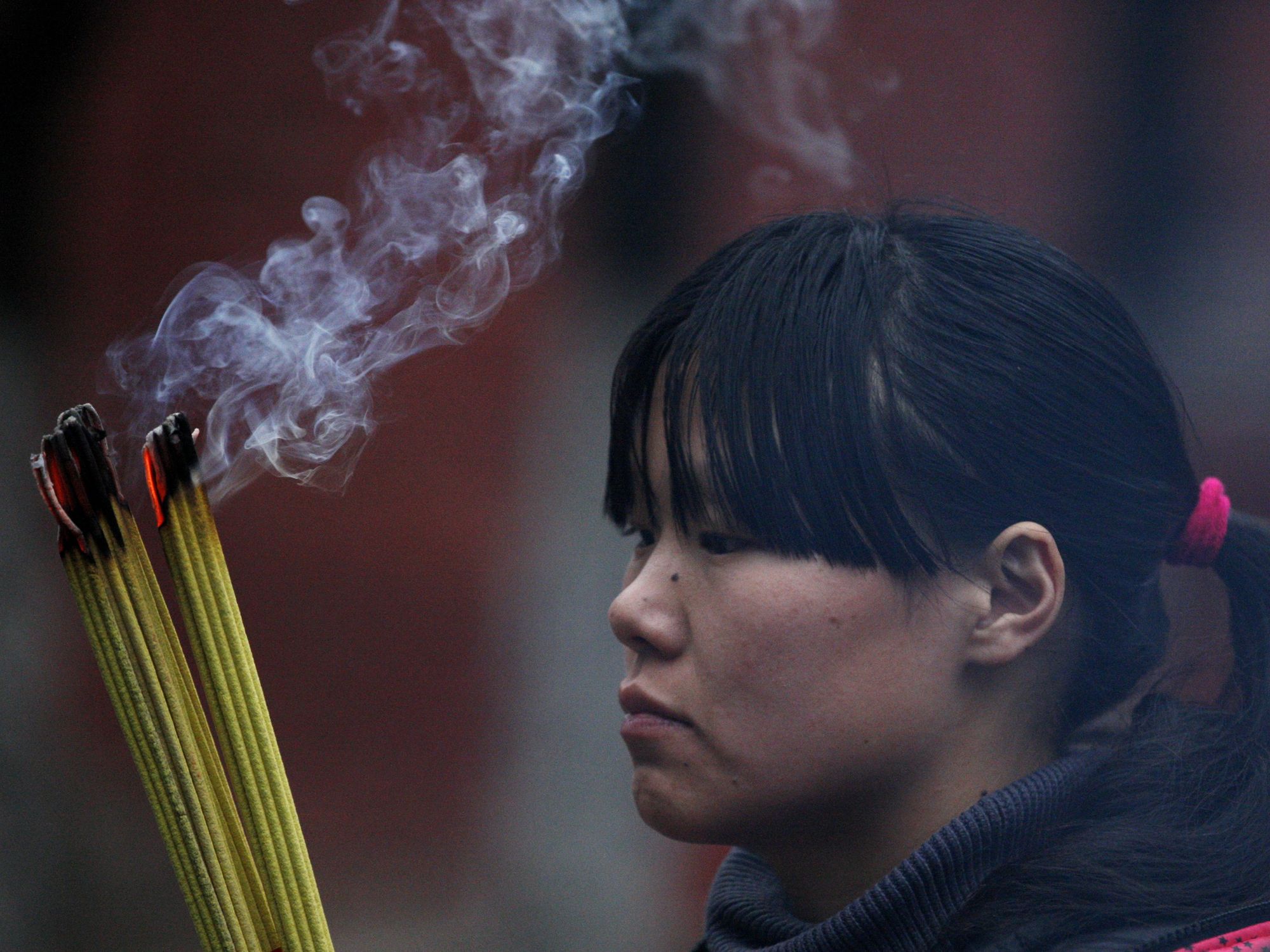 Photograph of a girl praying at a temple during Chinese Lunar New Year. She is burning incense.
