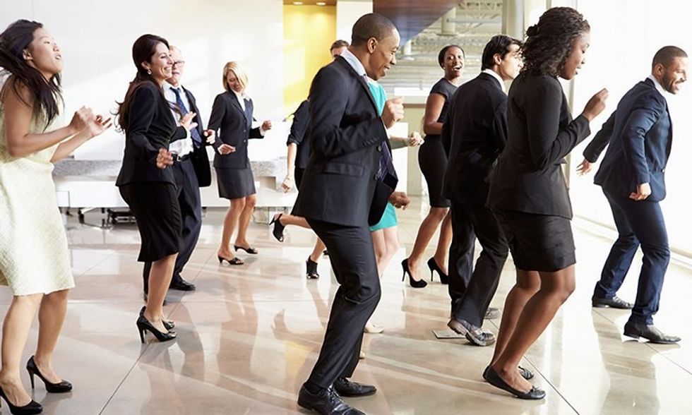 Photograph of a group of people dressed in office clothing dancing in line.