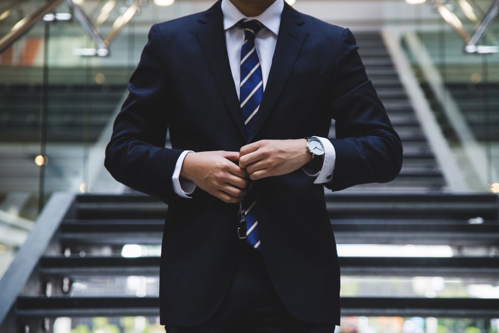 Photograph of a man fixing his suit at the bottom of fancy stairs,