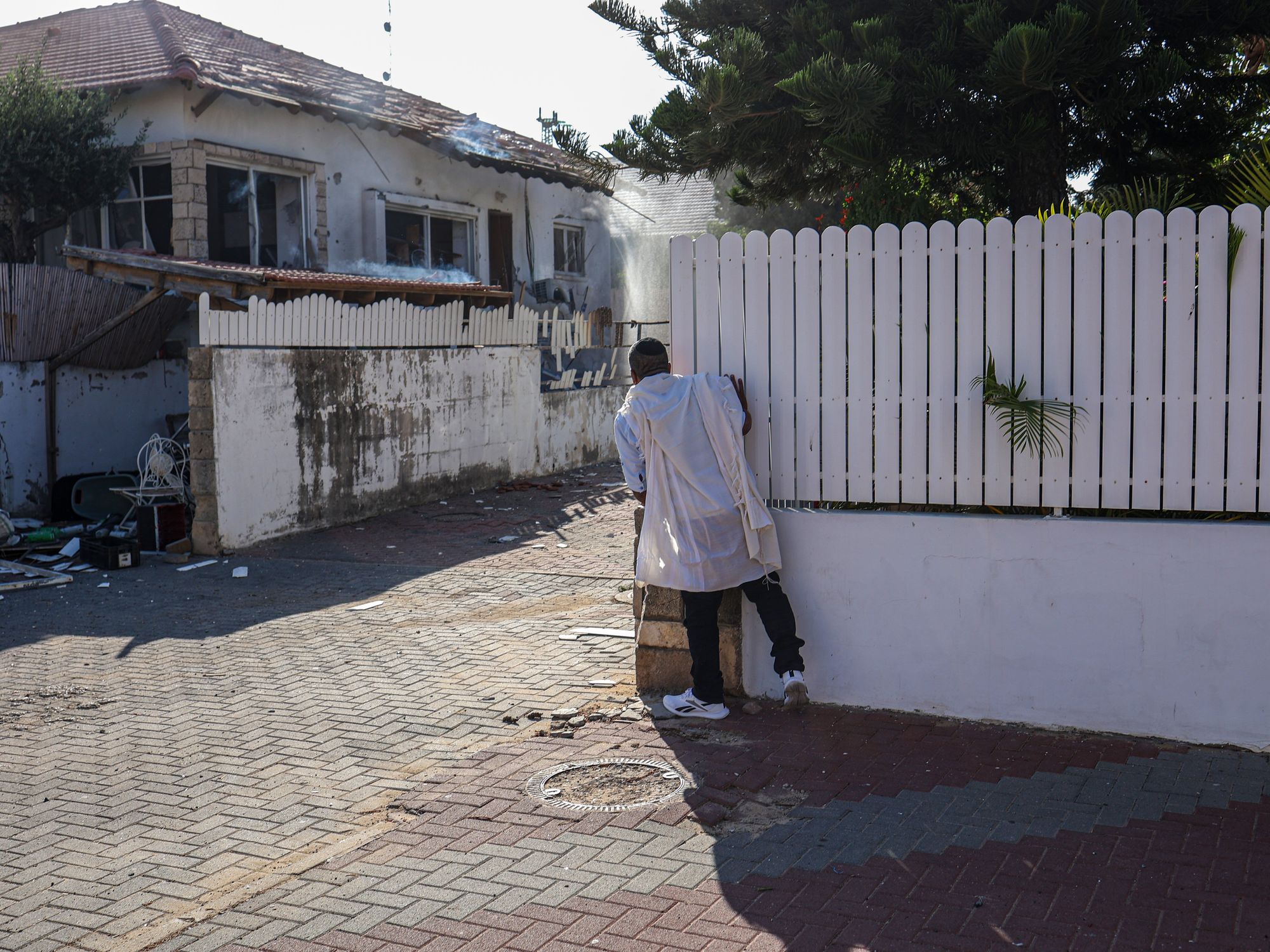Photograph of a man peeking around a corner to inspect the damage caused by a rocket attack from Gaza.