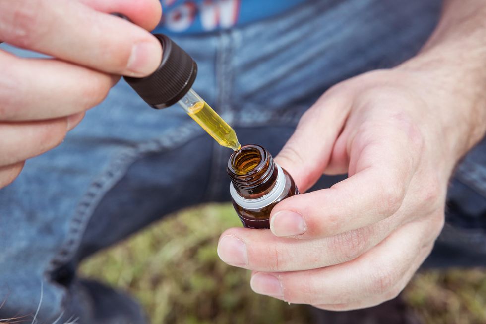 Photograph of a person holding a drop bottle of CBD oil