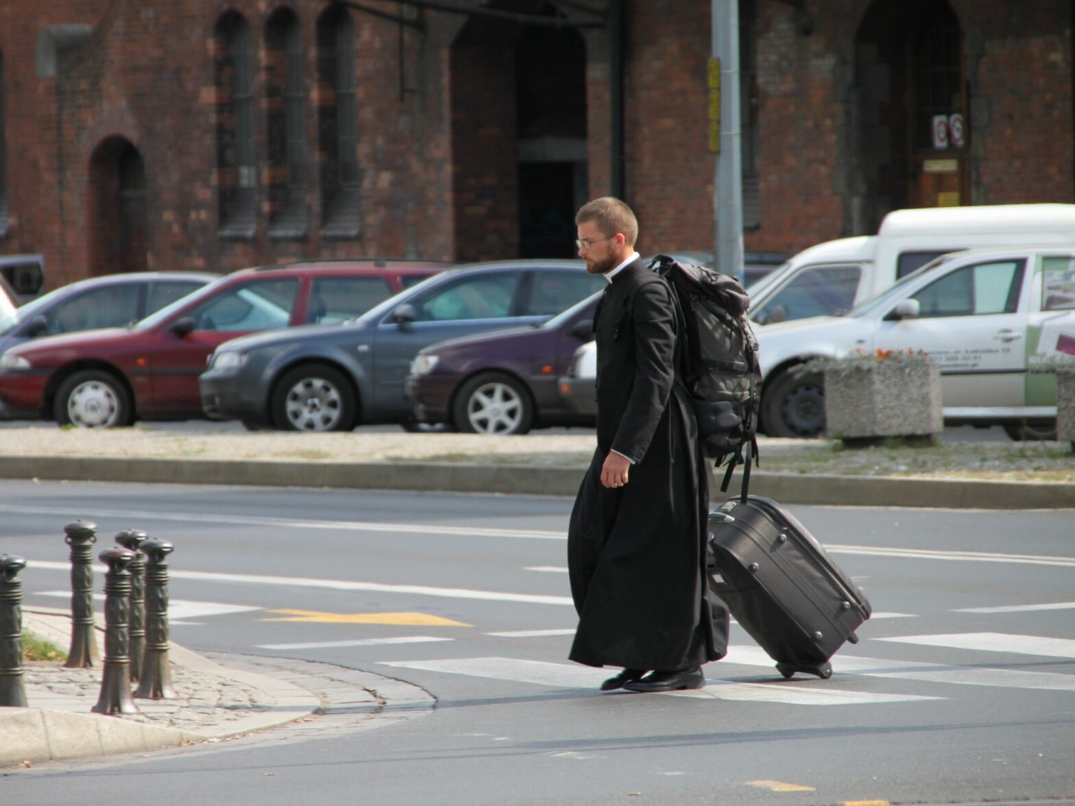 Photograph of a priest crossing the road with luggage in hand as he heads to Tumski Island, Poland.