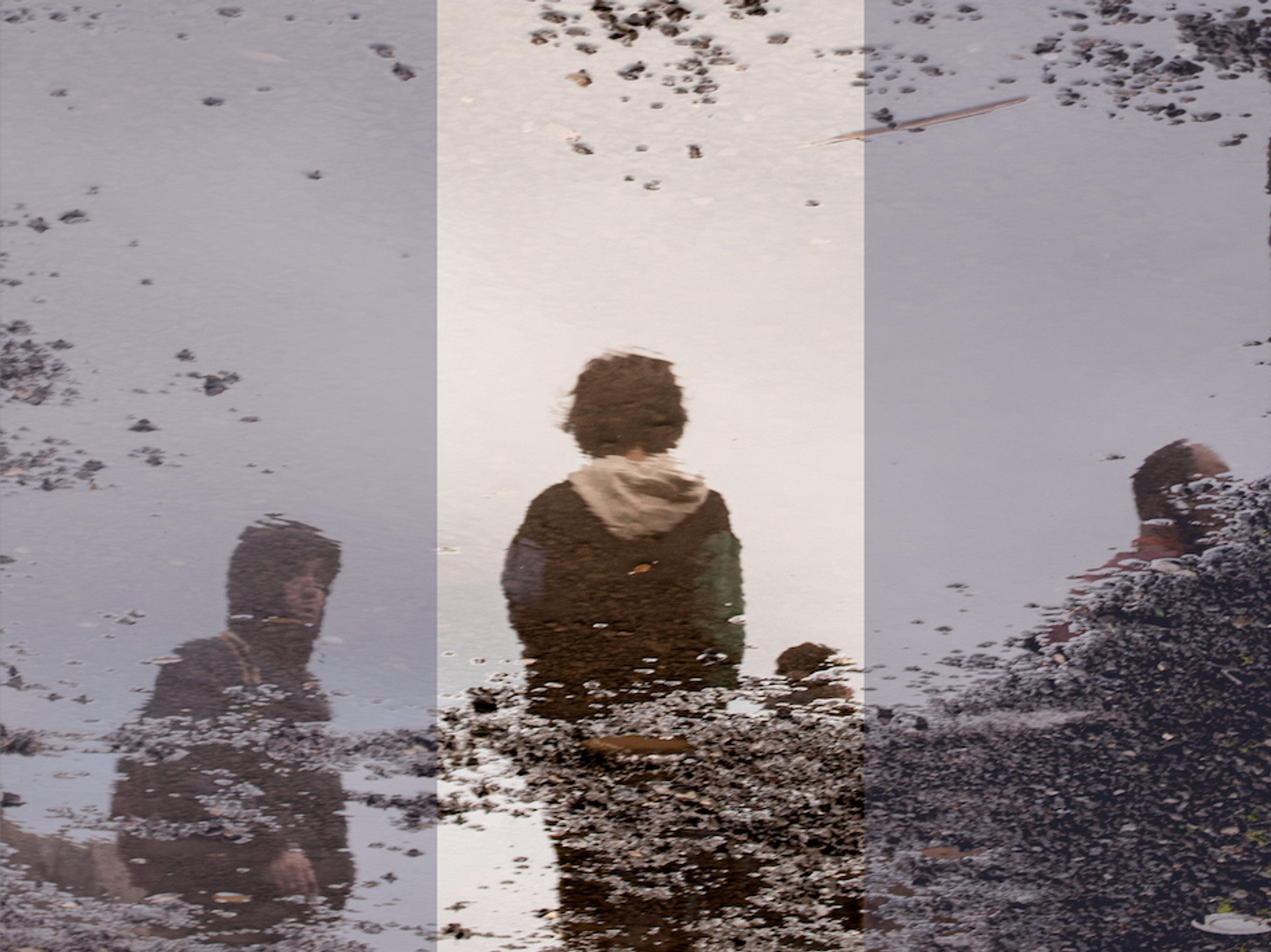 Photograph of a puddle's reflection, where children stand by the side of a gravel street
