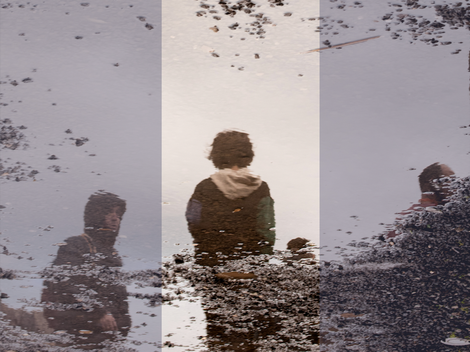 Photograph of a puddle's reflection, where children stand by the side of a gravel street